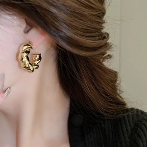 Close-up of gold twisted C-shaped hoop earrings featuring a stylish croissant metal texture