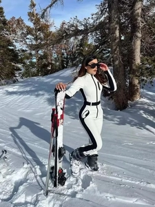 Combinaison de ski femme blanche avec bandes noires dans un paysage de montagne enneigé