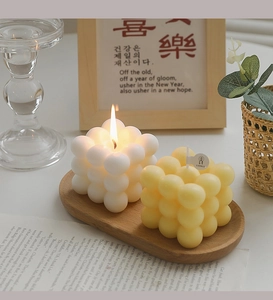 Macro view of burning bubble cube candles in cream and soft yellow on a wooden tray