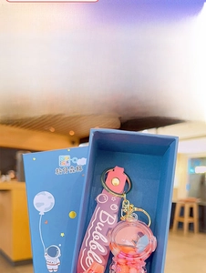 Detail of pink astronaut keychain with bubble strap next to blue cartoon gift box