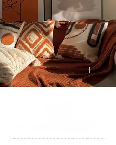 Detail of boho tufted pillow cases with geometric patterns and fringe decor on orange blanket