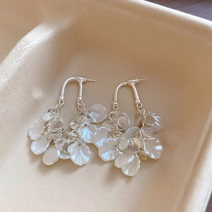 Détail des boucles d'oreilles à pampilles en nacre et argent sur un support beige doux