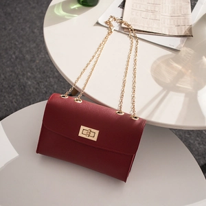 Fashionable wine red crossbody bag with gold chain strap on a minimalist white table