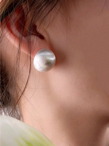 Close-up of a silver brushed metal ball earring worn by a model in a retro style