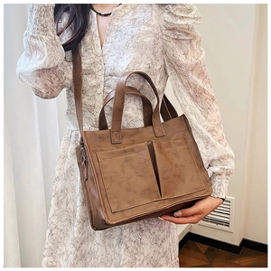 Brown vintage PU leather tote bag with dual front pockets worn as a crossbody bag