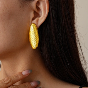 Macro side view of textured golden oval stud earrings with brushed metal finish on model