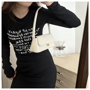 Chic cream-white baguette shoulder bag with gold hardware clasp held by a model