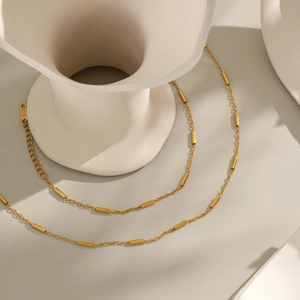 Dettaglio della collana placcata oro 18K con cilindri lucidi su un vaso di ceramica