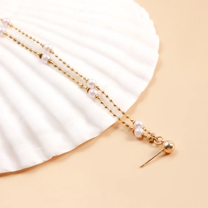 Détail de boucles d'oreilles pendantes dorées à pampilles avec perles sur un coquillage