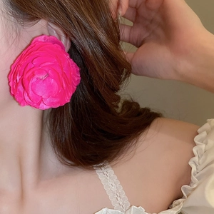 Close-up of oversized pink fabric flower tassel earrings worn by a model in daylight