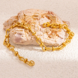 Close-up of gold braided leaf chain bracelet placed on a natural grey rock texture