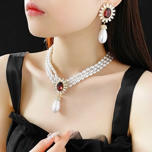 Close-up of triple-strand pearl necklace with oval ruby pendant and matching drop earrings
