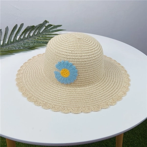 Détail d'un chapeau de paille beige avec bord ondulé et petite marguerite au crochet bleue