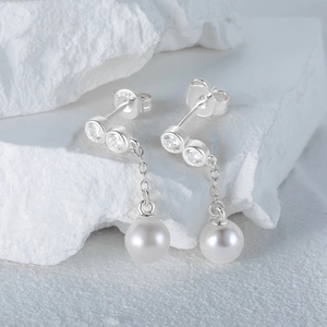 Macro detail of S925 silver earrings with zircon accents and pearl pendants on stone
