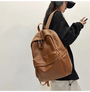 Side view of a vintage brown leather backpack worn by a model against a white wall