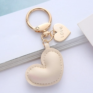 Detail of a beige leather heart keychain with gold 'Love' charm on white background