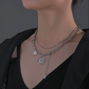 Detail of silver double-layered necklace featuring smiley face and letter B pendants