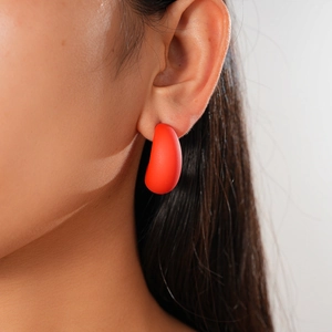 Close-up of a matte dark red C-shaped acrylic earring worn by a model in soft lighting