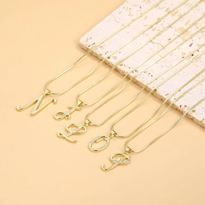 Detail shot of gold letter pendants M L O P with cubic zirconia on snake chain necklace