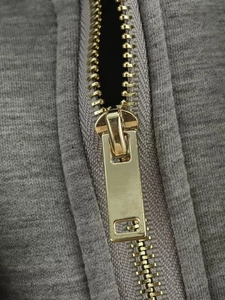 Detailansicht eines goldenen Metallreißverschlusses an einer grauen gesteppten Kapuzenjacke