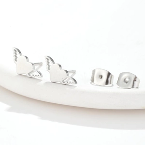 Macro detail of silver heart wing earrings and butterfly backings on a white surface