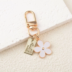 Detail view of gold flower keychain with Find Joy engraved plate on a white texture background