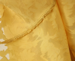 Makrodetail von gelbem floralem Jacquard-Stoff mit hochwertiger Kantennaht-Verarbeitung