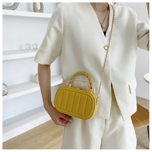 Detail of a bright yellow quilted box bag with a gold chain strap and twisted top handle