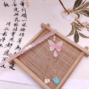 Dettaglio del fermaglio a farfalla in resina rosa con nappe e foglia di ginkgo dorata