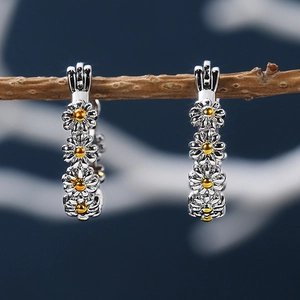 Macro view of silver daisy hoop earrings with gold centers on a rustic branch