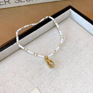 Macro shot of white seed bead necklace with gold shell pendant on a beige linen tray