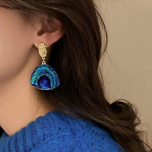 Close-up of irregular gold fan-shaped earrings with blue-green gradient crystal clusters
