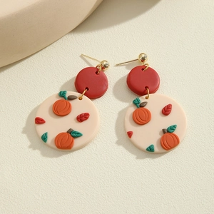 Close-up of handmade clay earrings featuring red studs and embossed orange pumpkin patterns