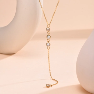 Golden stainless steel Y-shaped necklace with round cubic zirconia tassels on a white stand