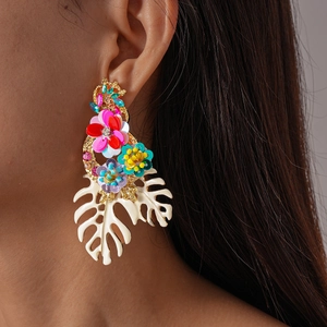 Close-up of oversized tropical floral earrings with rhinestones and Monstera leaf