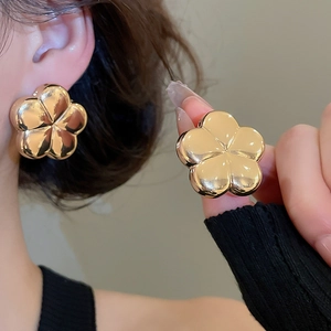 Close-up of large golden floral earrings with polished mirror finish on a female model