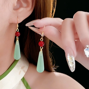 Detail of red bead and light green resin drop earrings worn by a female model