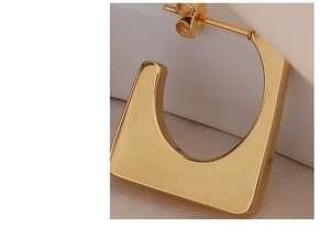 Macro shot of U-shaped gold earrings with brushed metallic texture and minimal geometry
