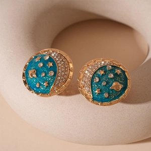 Close-up of star and moon earrings with blue enamel, gold planet, and sparkling rhinestones