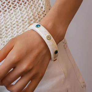 Detailed macro view of wide marble acrylic bangle with colorful rhinestones in gold setting
