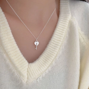 Close-up of minimalist 925 silver heart lock and key necklace worn on a cream sweater