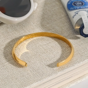 Detailed view of polished 18K gold-plated stainless steel open cuff on textured book