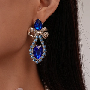 Detail view of crystal bow and blue water drop earrings worn by a model in close-up