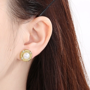 Close-up of elegant gold pearl stud earring with pavé diamonds worn by a model