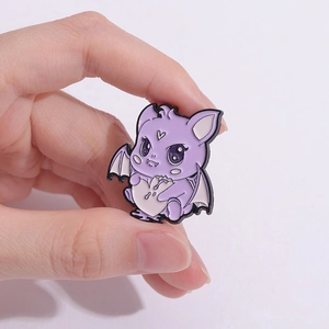 Cute purple cartoon bat enamel pin with heart detail held in hand for size visualization