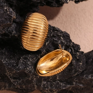 Detailed view of gold oval earrings with horizontal stripes on a textured stone surface