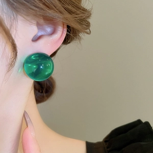 Gros plan d'un modèle portant une boucle d'oreille sphérique en résine verte translucide