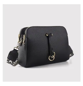 Detail view of black lychee grain crossbody bag with woven strap and gold ring decor