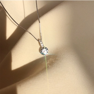 Macro shot of 925 silver water drop pendant with sparkling zircon on champagne silk fabric