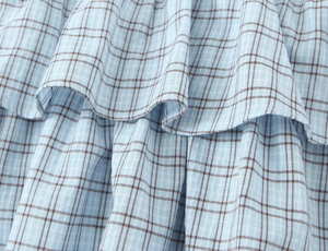 Close-up of light blue plaid fabric featuring layered ruffle details and woven texture